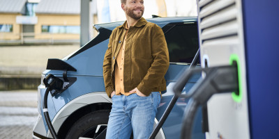 Homme se tenant à coté d'une voiture électric en charge chez Q8 electric