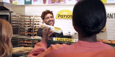 Un employé de Panos remet un sandwich Panos à un client au comptoir.