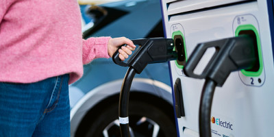 Femme avec pull rose prenant le chargeur pour sa voiture a une borne de recharge Q8 electric