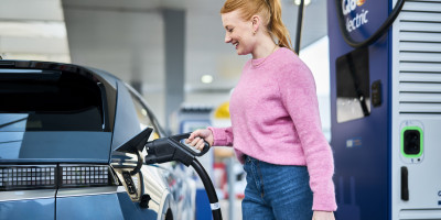 Une femme branche un chargeur sur sa voiture électrique au Q8 electric